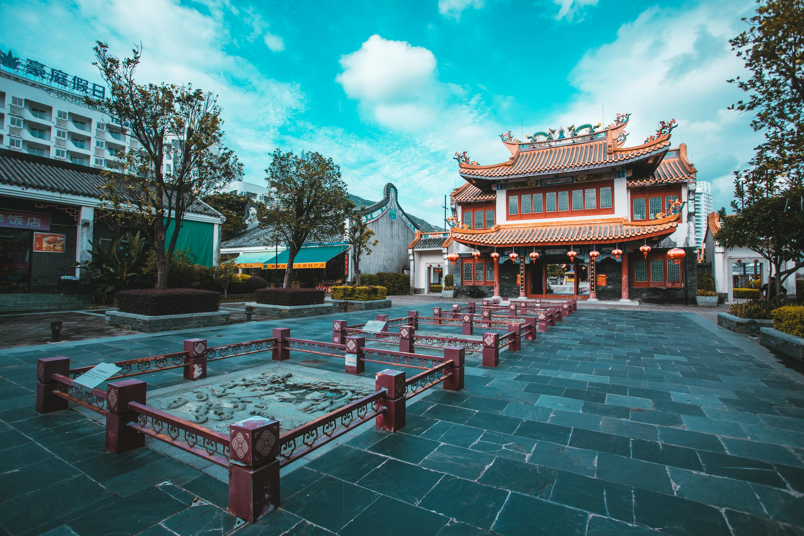 A vibrant view of traditional Chinese buildings in an outdoor plaza with trees and lanterns.