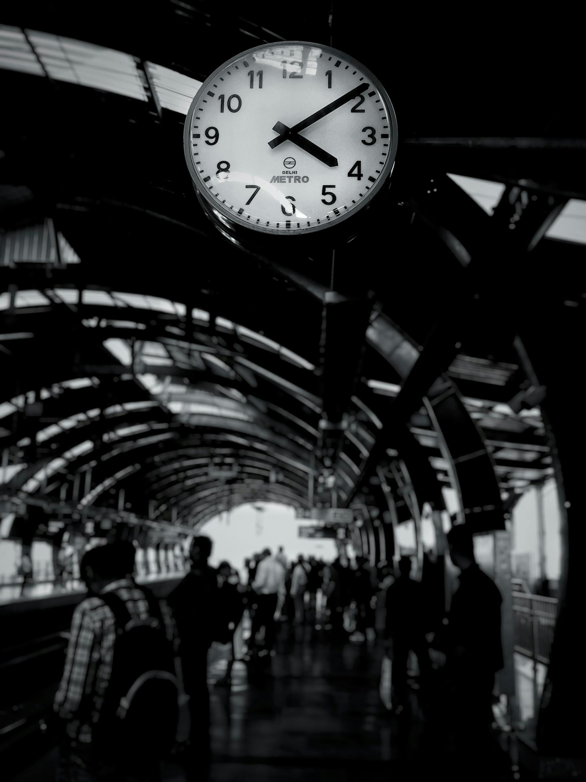 Black and white photo of a bustling metro station with a prominent clock and commuters.